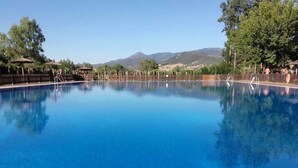 Una piscina blu cristallina con bordo piastrellato, circondata da una recinzione in legno e alberi, con montagne sullo sfondo.