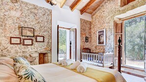 A bedroom with stone walls, a bed with a yellow blanket, and a balcony with a wooden railing.