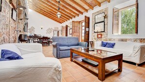 A spacious living area with a high wooden ceiling, a dining table with chairs, a blue sofa, and a white sofa with blue cushions.