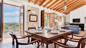 A dining area with a wooden table set for four, surrounded by chairs, with a view of the outdoors.