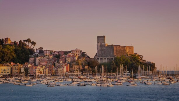 Une ville côtière dotée de bâtiments historiques, d’un imposant beffroi et d’un port de plaisance rempli de bateaux.