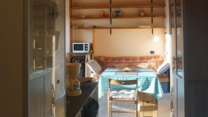 Une cuisine équipée d’un four à micro-ondes, une table recouverte d’une nappe à carreaux et une chaise. On y trouve également un meuble avec des portes en verre et un tapis sur le sol.