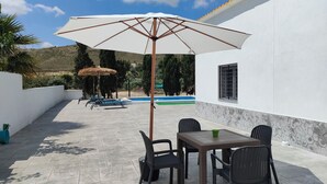 Een terras met een tafel, stoelen, een grote parasol en een zwembad op de achtergrond.