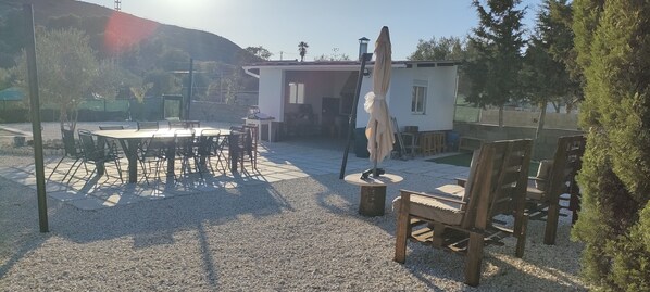 A patio area with a round table and chairs, a small building with a window, and a ladder.