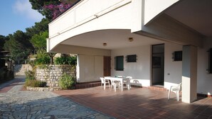 Un patio con suelo de piedra, una mesa con sillas y una pared de piedra con plantas.