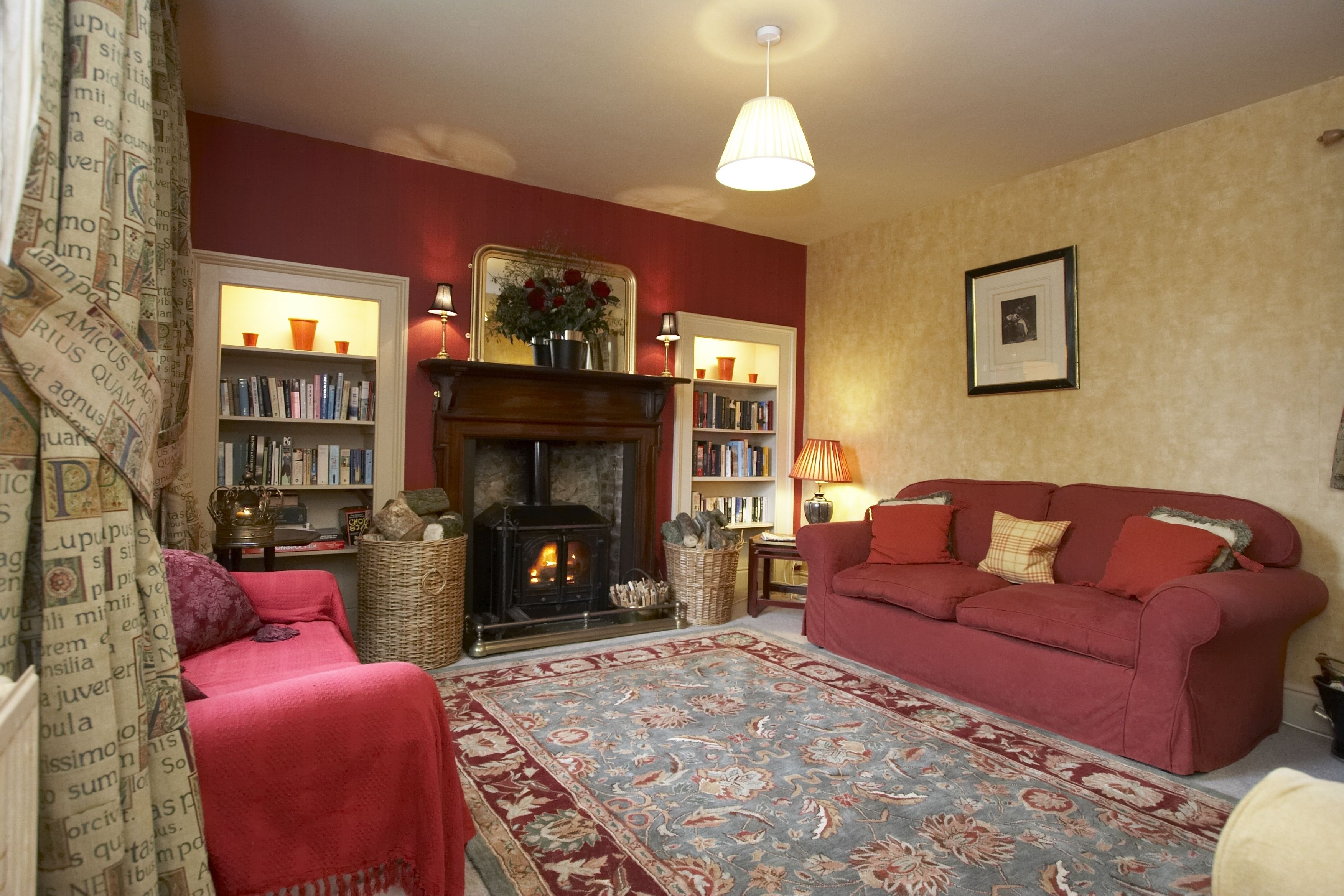 A cozy living room with a fireplace, bookshelves, a red sofa, and a patterned rug.