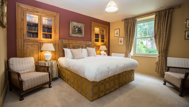 A bedroom with a large bed, two bedside tables with lamps, a wooden wardrobe, and a window with curtains. - The Cornmill (York)