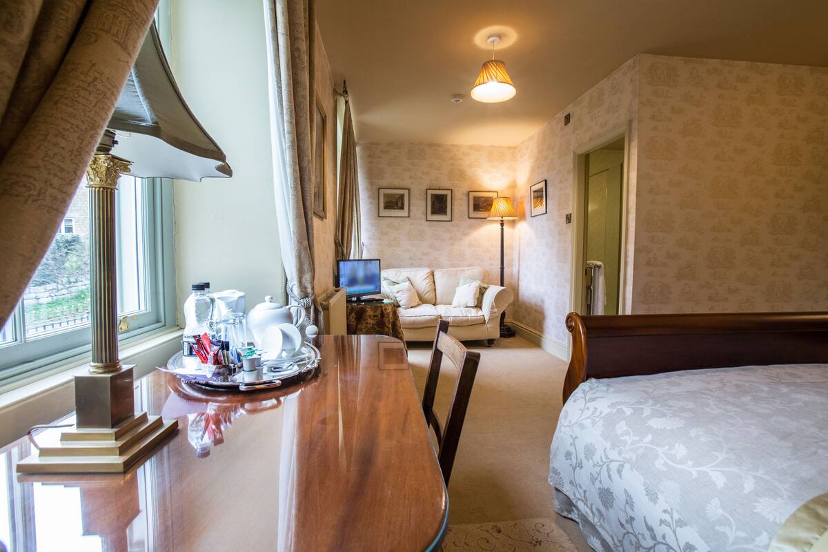 A hotel room with a wooden dining table, a sofa, a bed, and a television.