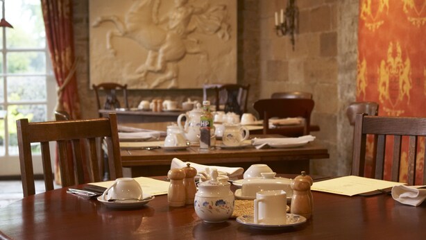 A dining table set with tea service, chairs, and a stone wall with a mural.