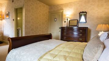 A neatly made bed with a quilted cover, a wooden dresser with a mirror, and a door leading to another room.