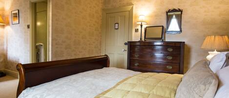 A neatly made bed with a quilted cover, a wooden dresser with a mirror, and a door leading to another room.