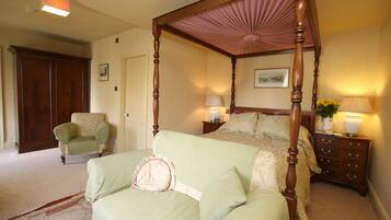 A four-poster bed with a canopy, a nightstand with lamps, a chair, and a door in a bedroom.