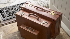 Two brown leather suitcases with metal clasps and handles, placed on a stone floor near a door.