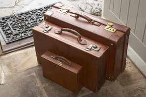 Two brown leather suitcases with metal clasps and handles, placed on a stone floor near a door.