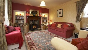 A cozy living room with a fireplace, red sofas, a bookshelf, and a patterned rug. - The Cornmill (York)