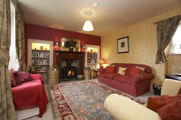 A cozy living room with a fireplace, red sofas, a bookshelf, and a patterned rug.
