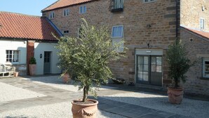 A stone building with a tiled roof, a balcony, and potted plants in the courtyard. - The Cornmill (York)
