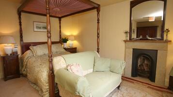 A four-poster canopy bed with a green upholstered sofa, a bedside table with lamps, a fireplace, and a mirror above it.