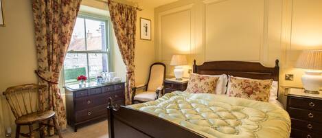 A bedroom with a large bed, a wooden nightstand, a chair, a dresser, and a window with curtains.