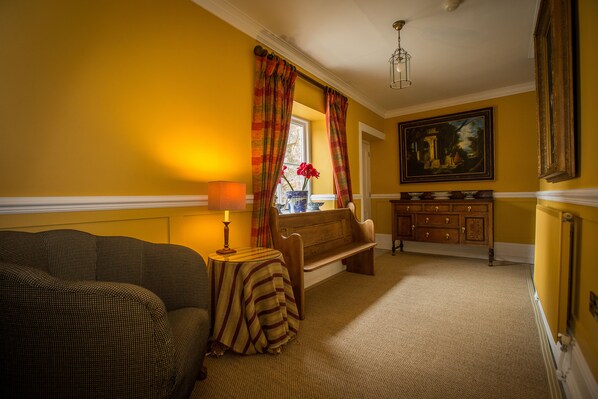 A room with a sofa, a small table with a lamp, a bench, a window with curtains, a cabinet, and a painting on the wall.
