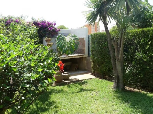 Un jardín con patio, una palmera y diferentes arbustos.