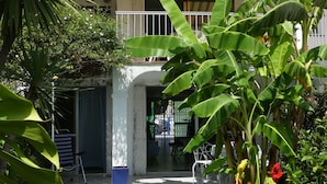 Un edificio de dos pisos con balcón, rodeado de abundante vegetación y un césped cuidado.