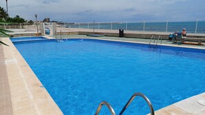Una piscina con agua azul cristalina, una silla de salvavidas y vista a la playa y al océano al fondo.