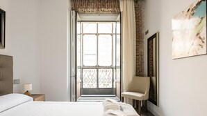 A hotel room with a large bed, a chair, a desk with a lamp, and a view through a window with a metal gate. - PUERTA DEL SOL CITY CENTER WITH BALCONY (Madrid)