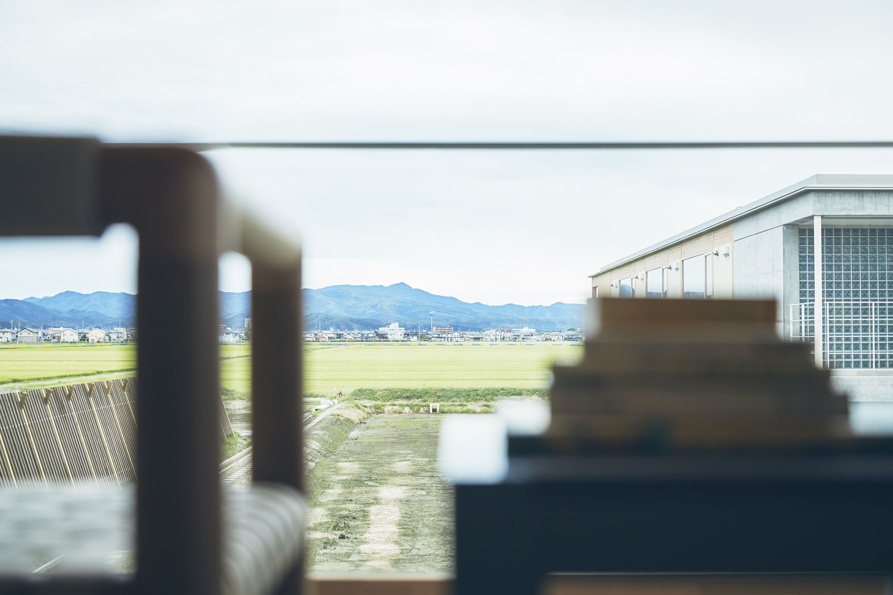 A view from a window overlooking a green field, a building, and mountains in the distance.