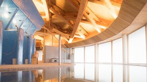 A spacious indoor swimming pool with clear blue tiles, wooden beams, and large windows.