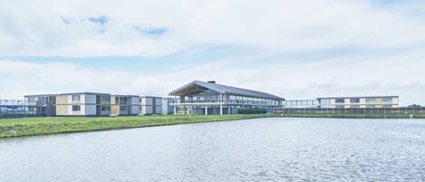 A modern building with a flat roof and large windows, situated next to a calm body of water.