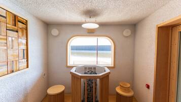 A small, cozy room with a large window, a wooden stool, a small table, and a wooden cabinet.