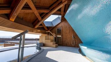 Un spa modern amb una banyera d'hidromassatge tancada amb vidre, bigues de fusta i vista a les muntanyes.