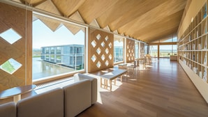 A spacious reading area with a high ceiling, large windows, and a view of a modern building.