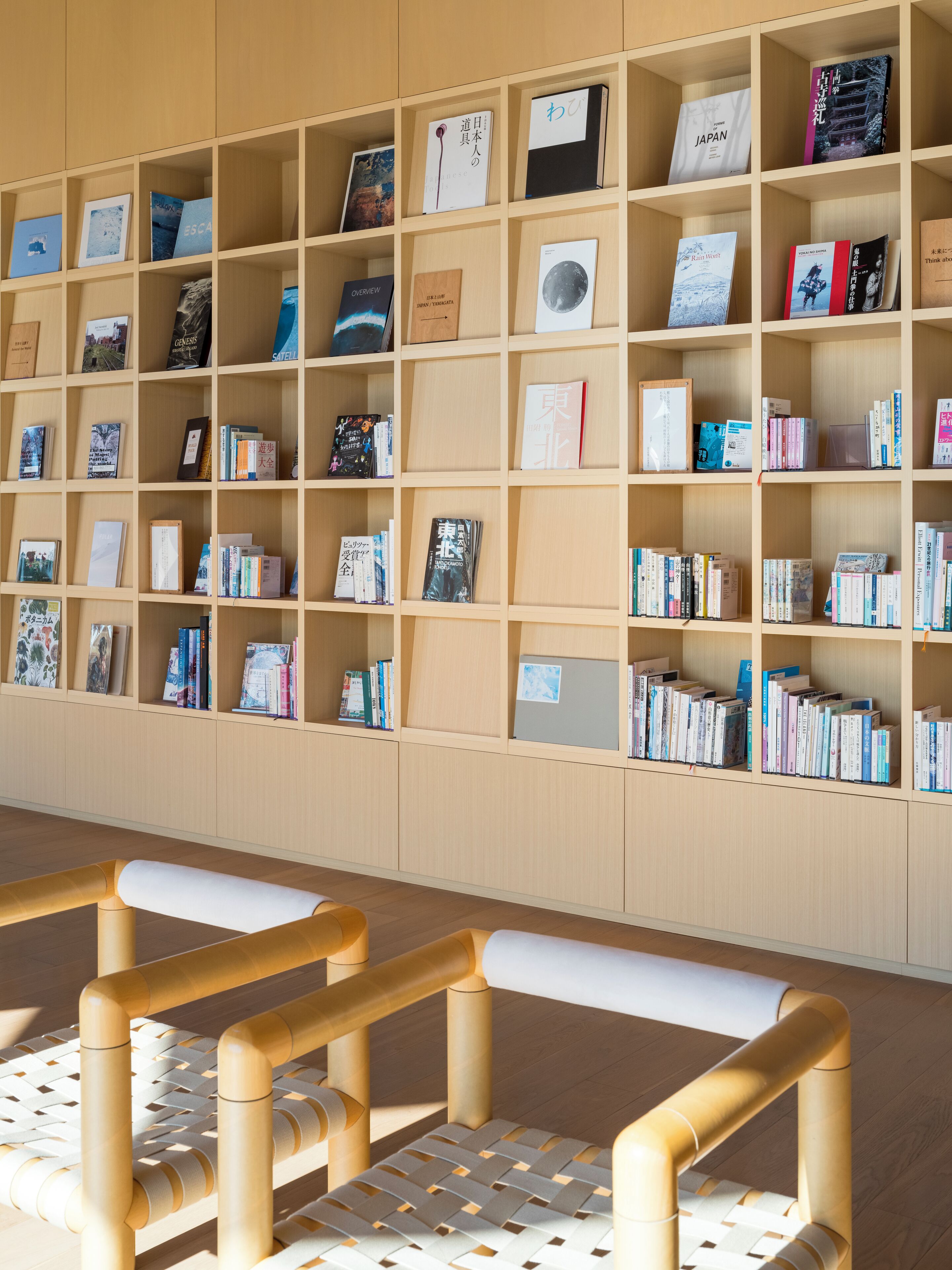 Una biblioteca con scaffali in legno pieni di libri e riviste. In primo piano, due poltrone di legno.