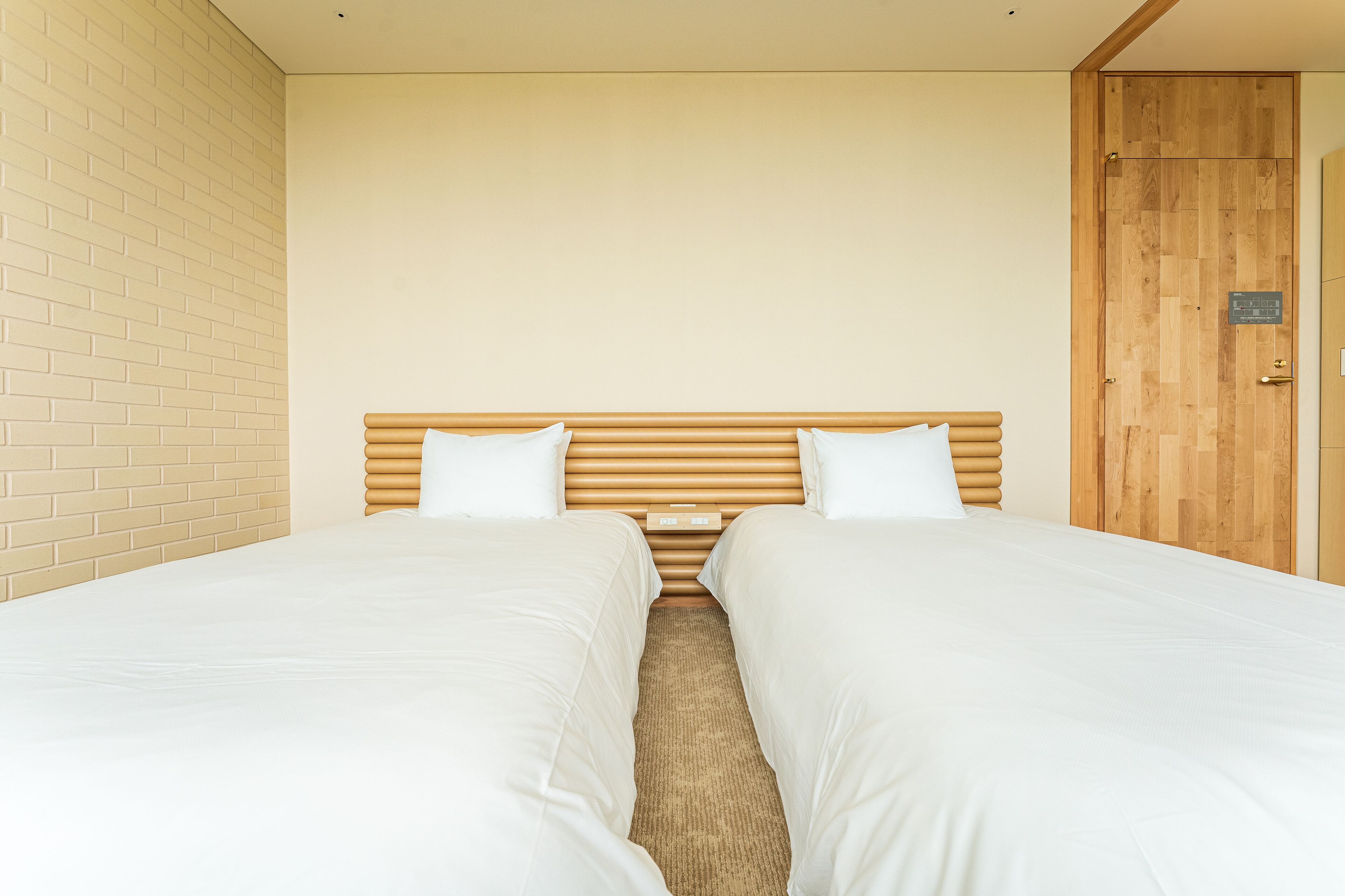 A room with two single beds, a wooden headboard, a brick wall, and a wooden door.