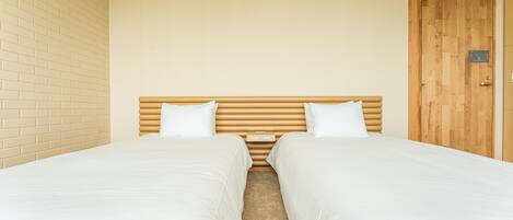 A room with two single beds, a wooden headboard, a brick wall, and a wooden door.