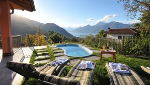 A swimming pool with lounge chairs and a table, surrounded by a deck and mountain views. - Clubhouse, Menaggio, Italy (Menaggio)