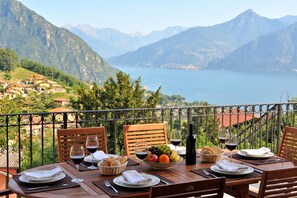 A table set with plates, glasses, and a bottle, overlooking a lake with mountains in the background.