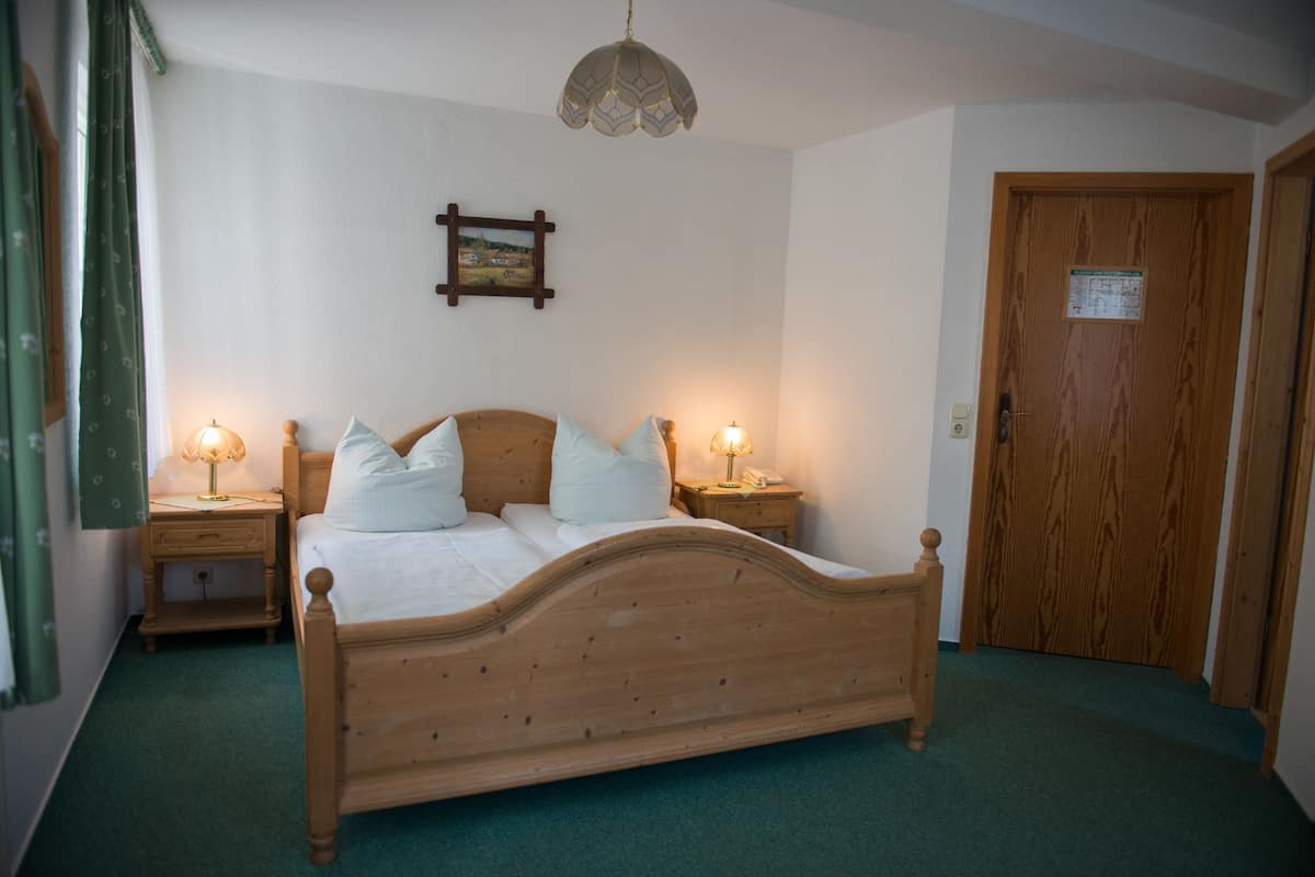 Ein Schlafzimmer mit einem hölzernen Bett, zwei Nachttischen mit Lampen, einer Holztür und einem an der Wand hängenden Bild.