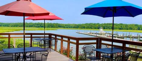 A deck with tables and chairs, overlooking a body of water and a dock.