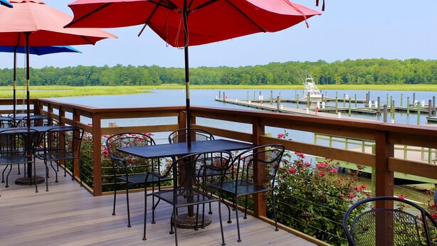 A deck with outdoor seating, red umbrellas, and a view of a lake and dock.
