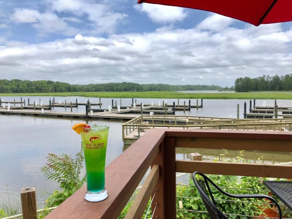 A view of a lake with docks, a wooden deck, and a glass of a green beverage with a garnish.