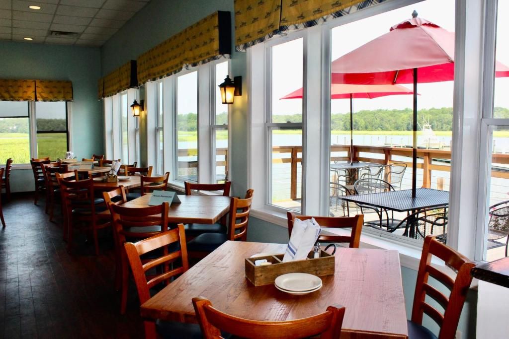 An indoor dining area with tables and chairs, large windows, and a view of the outdoors.