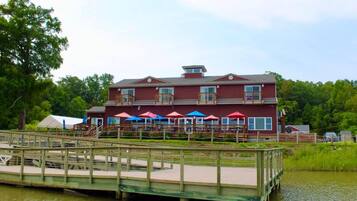 A waterfront property with a dock, a building with multiple balconies, and outdoor seating with umbrellas.