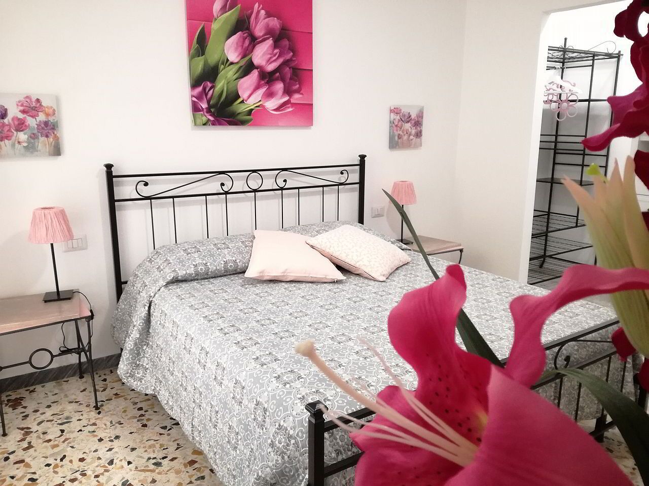 Une chambre à coucher avec un lit, une table de chevet, une lampe et un mur orné d’un tableau représentant des motifs floraux.