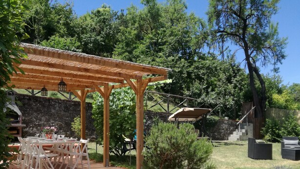 A wooden pergola with a table and chairs underneath, surrounded by greenery and trees. - Chianti Best House - Comfort, relax & privacy in the center of Greve in Chianti (Greve in Chianti)