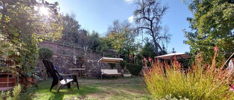 Un jardín con mesa y sillas, una pérgola y diversas plantas.