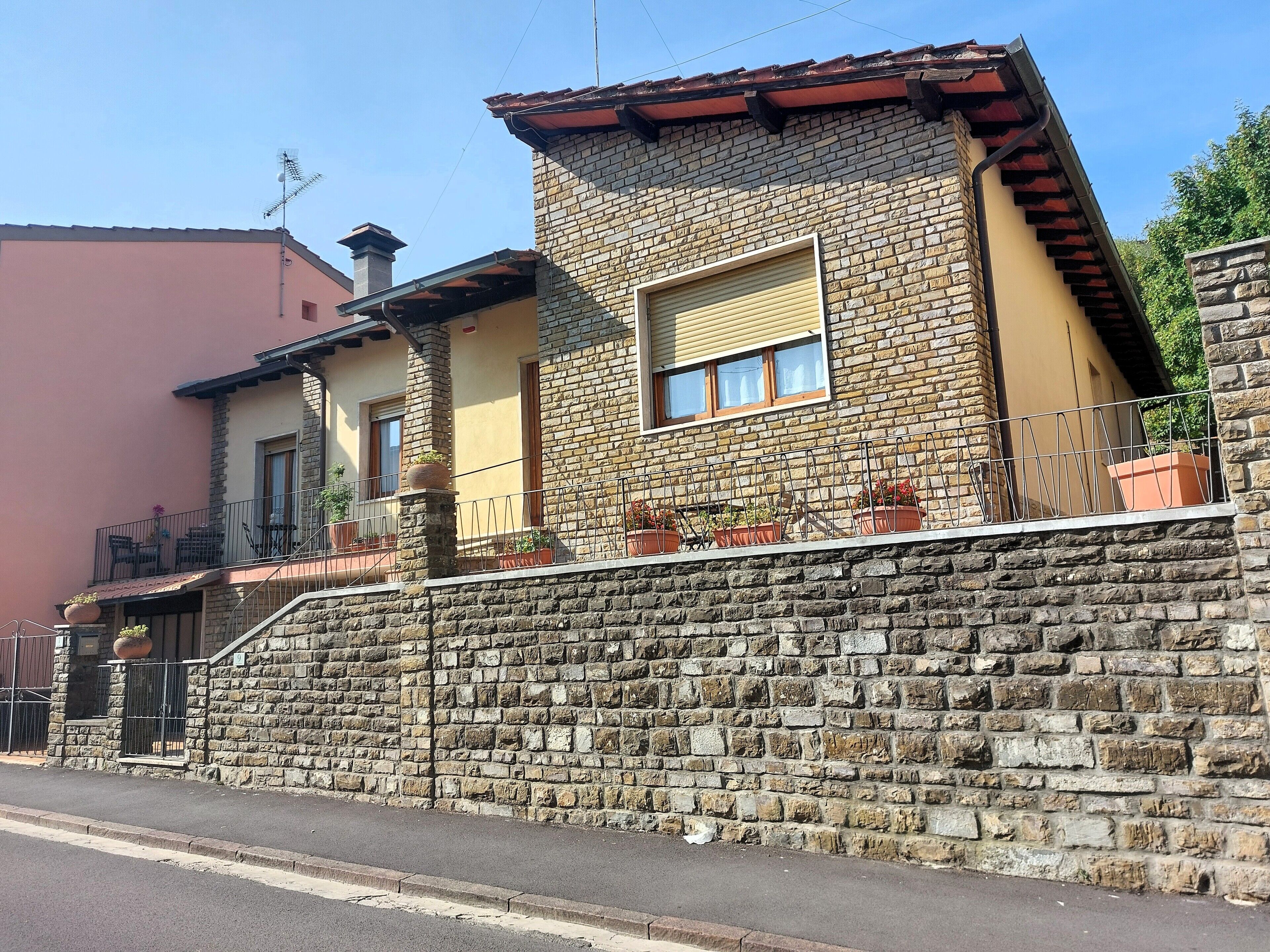 A stone-walled building with a balcony, a window with shutters, and a small garden area.
