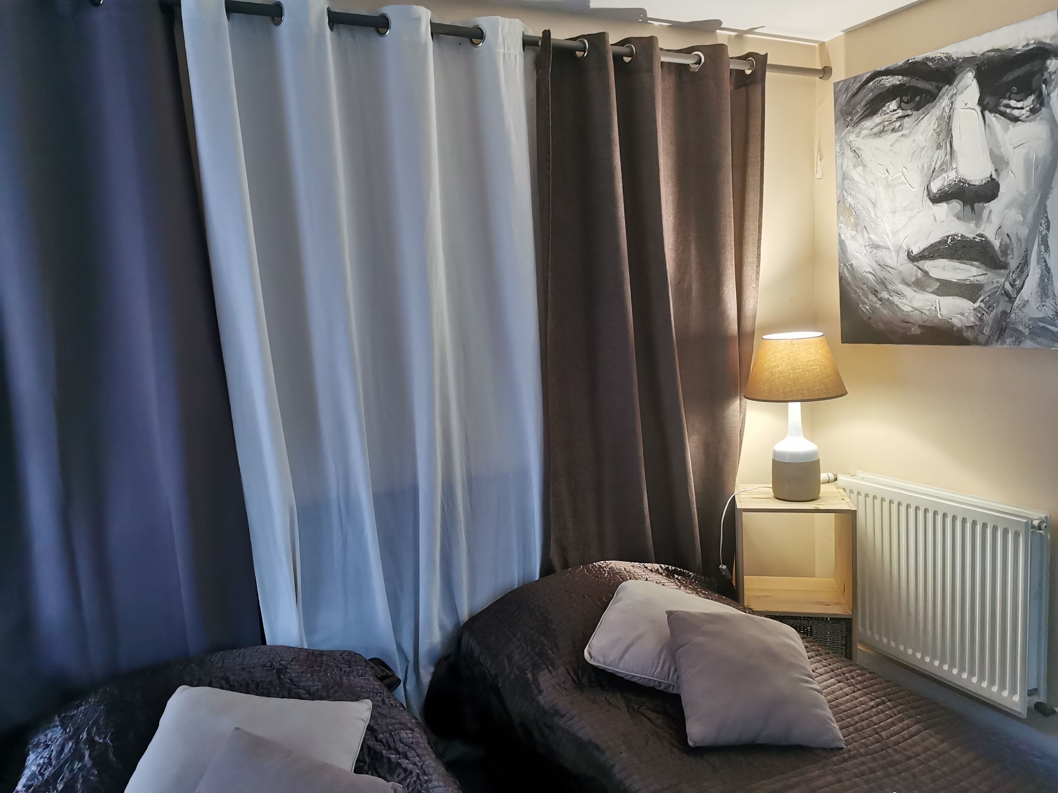 Ett sovrum med två sängar, en lampa, ett element och en tavla på väggen.